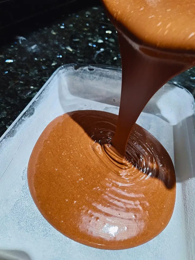 Pouring smooth, velvety easy chocolate blender cake batter into a floured glass baking dish to make a traditional Moroccan Meskouta.
