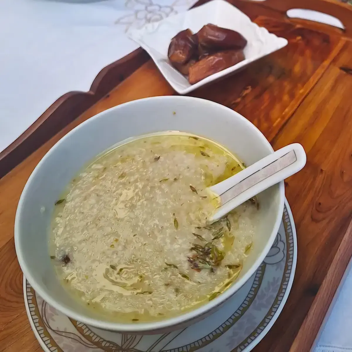 A square overhead shot of creamy Moroccan Barley Soup (Hassoua) served on a rustic tray with a side of sweet dates for a traditional breakfast.