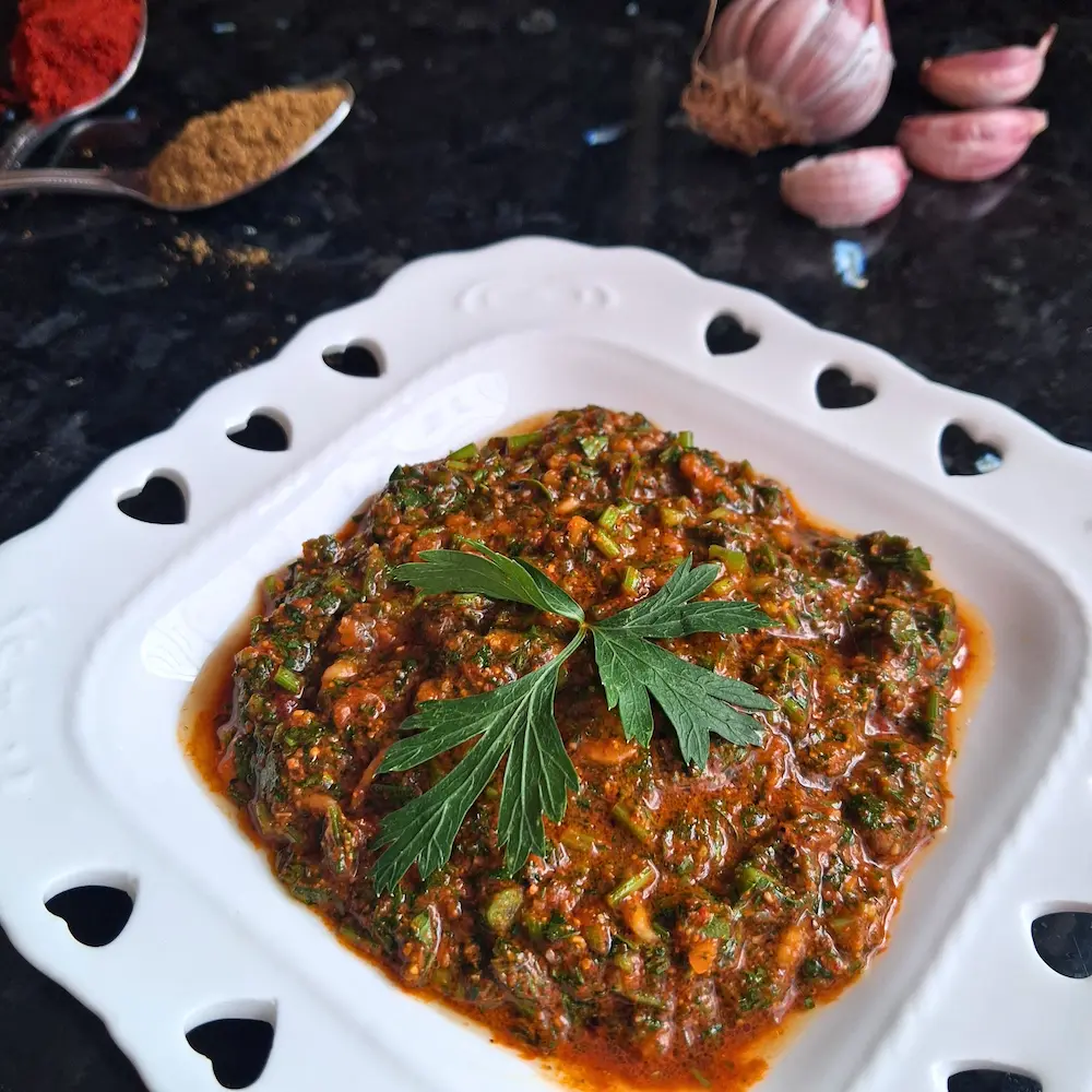 A close-up of freshly made authentic Moroccan Chermoula, a vibrant green and red herb marinade glistening with olive oil, served in a white bowl and garnished with fresh parsley.