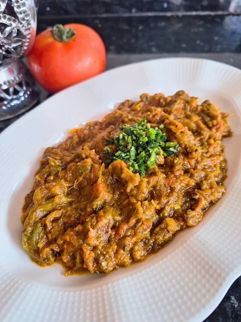 Zaalouk_vertic A beautifully plated serving of authentic Moroccan Zaalouk on a clean white dish, highlighting its rich, jammy texture and a fresh drizzle of extra virgin olive oil.