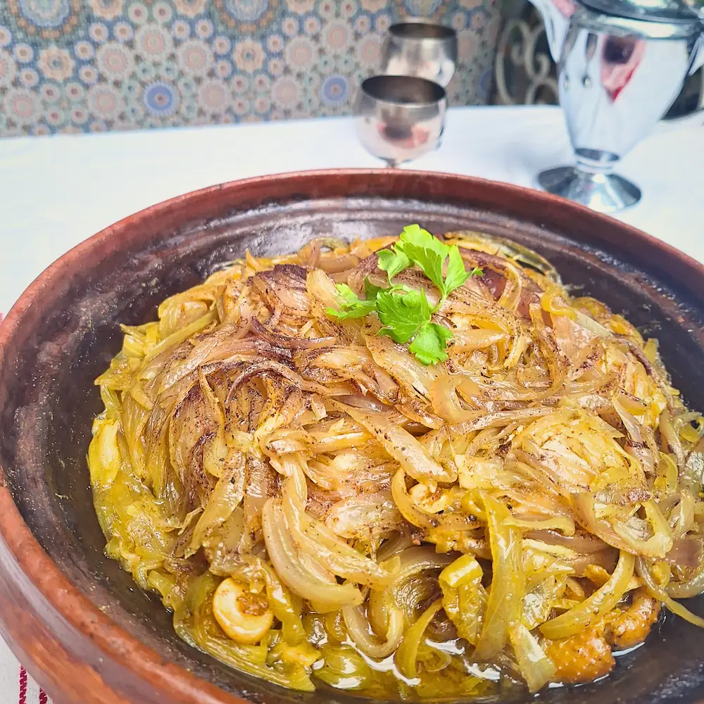 A close-up of a freshly cooked Chicken Tagine with Caramelized Onions in an open clay pot, featuring melt-in-your-mouth chicken and a thick, savory-sweet onion glaze.