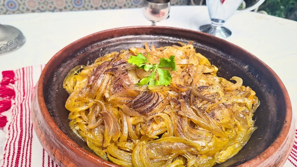 A horizontal view of our authentic Chicken Tagine with Caramelized Onions, showing tender, slow-cooked chicken smothered in a thick, golden saffron and cinnamon glaze inside a traditional pot.