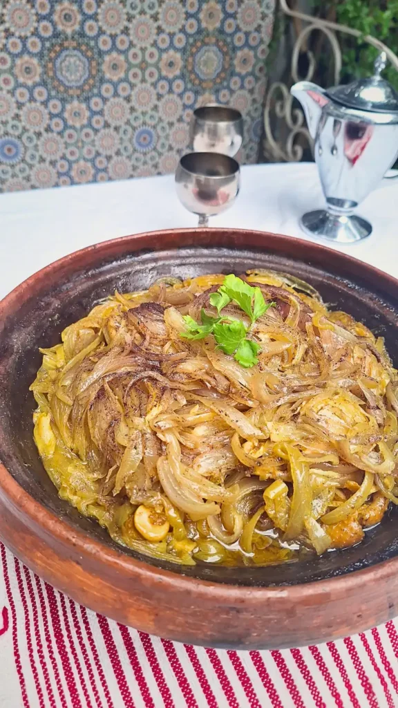 A close-up of a freshly cooked Chicken Tagine with Caramelized Onions in an open clay pot, featuring melt-in-your-mouth chicken and a thick, savory-sweet onion glaze.