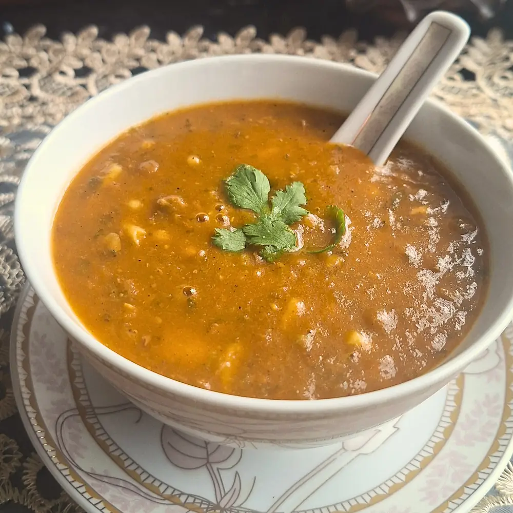A close-up of authentic Moroccan Harira, a rich and hearty tomato, chickpea, and lentil soup, served in a white bowl and garnished with fresh cilantro.