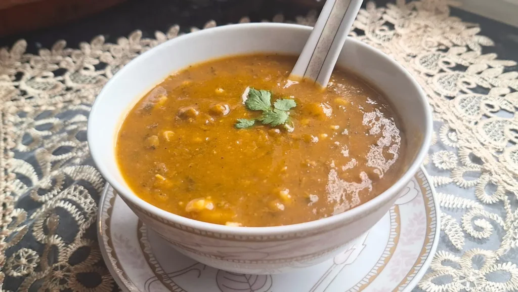A steaming bowl of authentic Moroccan Harira soup filled with hearty chickpeas and lentils, garnished with a fresh cilantro leaf and served on a traditional lace tablecloth.