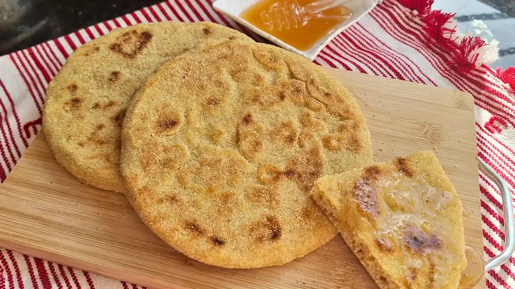 A close-up of authentic Moroccan Batbout, a fluffy stovetop semolina pan bread, served warm on a wooden cutting board with a wedge drizzled in golden honey.